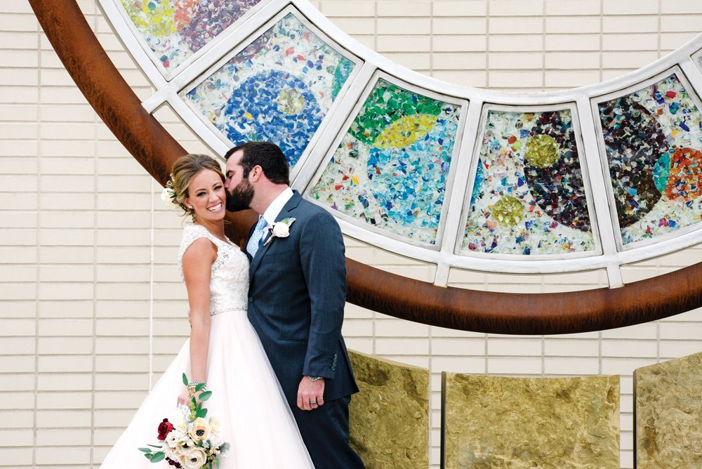 Happy wedding couple kissing in front of PACE Center outdoor art in Parker, CO.