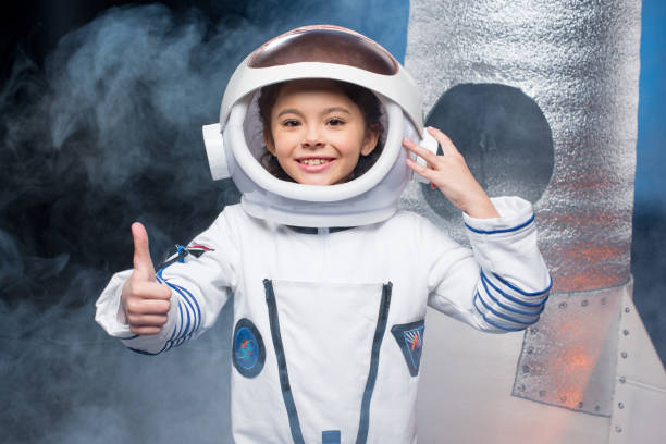 Cute little girl in astronaut costume showing thumb up and smiling at camera