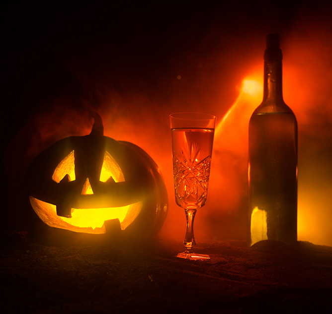 Halloween wine party theme. Glass of wine and bottle with Halloween - old jack-o-lantern on dark toned foggy background. Scary Halloween pumpkin