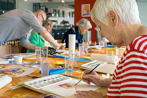 Adult Artwatercolor painting at table with other students in spacious studio.