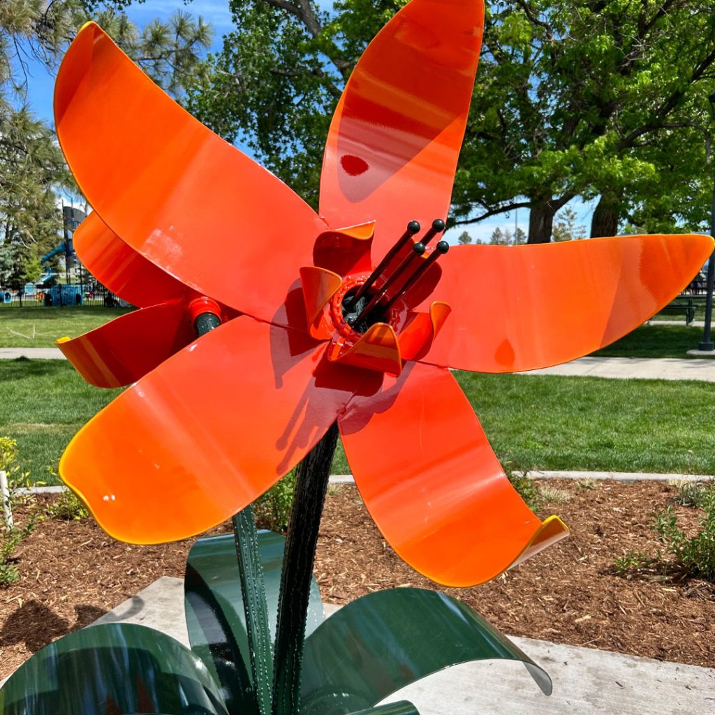 Large outdoor metal flower sculpture with orange blossoms and green stem