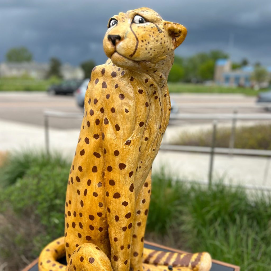 Large outdoor sculpture of cheetah sitting on perch.