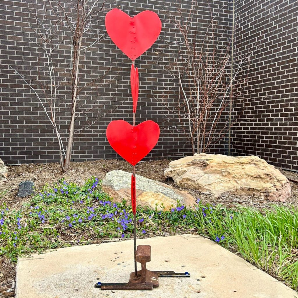 Large outdoor metal sculpture of three red hearts stacked on top of one another.