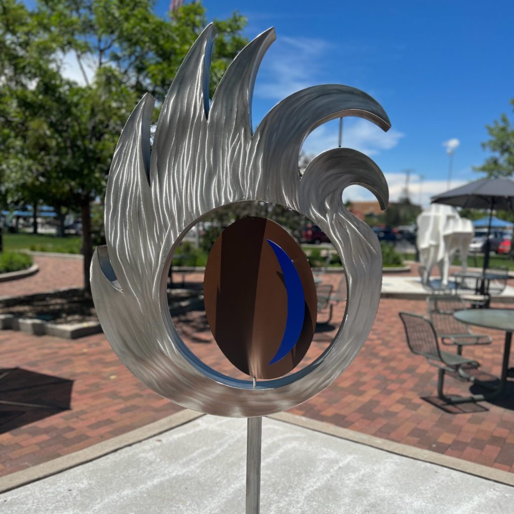 Large outdoor metal sculpture of sun with rotating moon inside it.