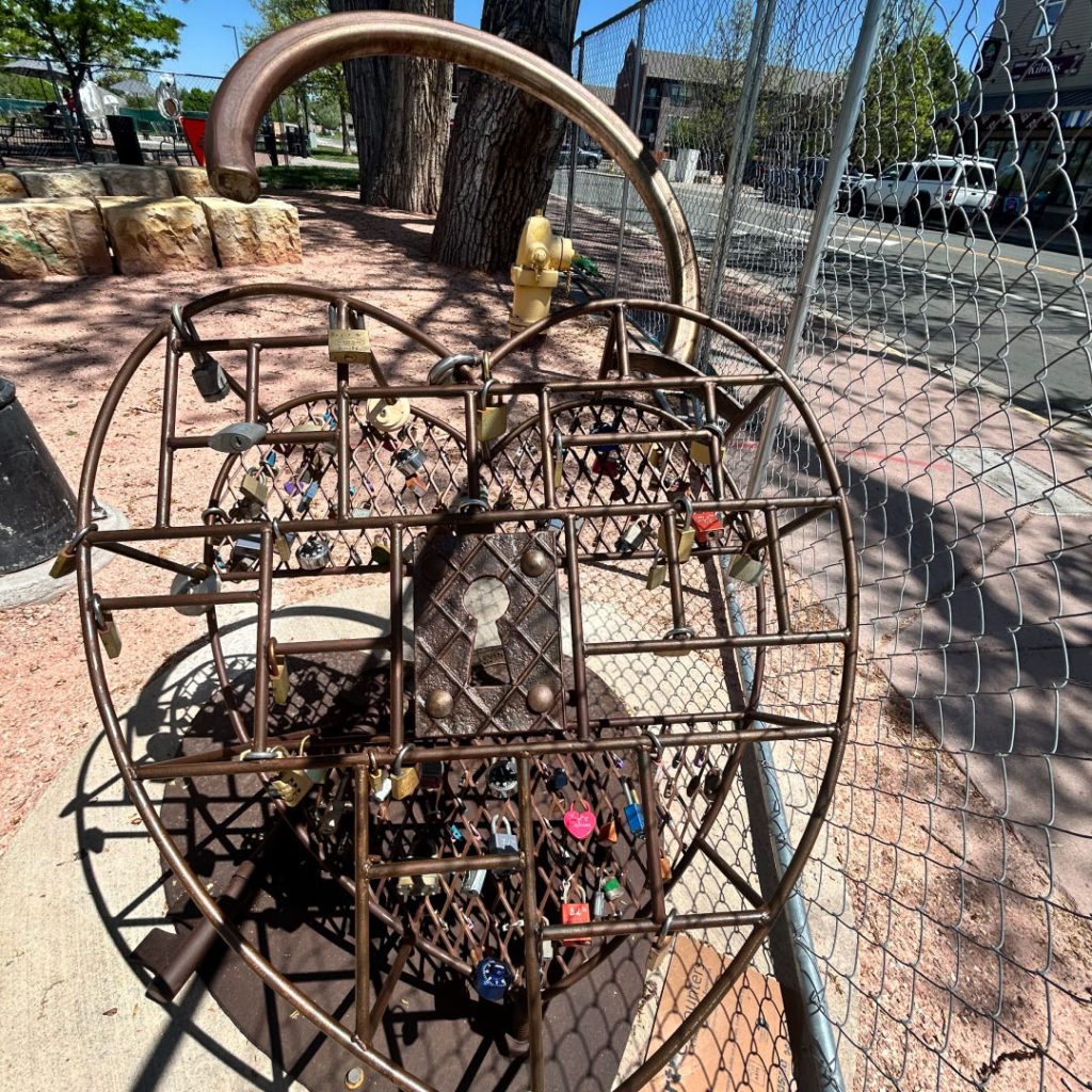 Large outdoor sculpture of a metal hear lock with individual, smaller locks attached to it.