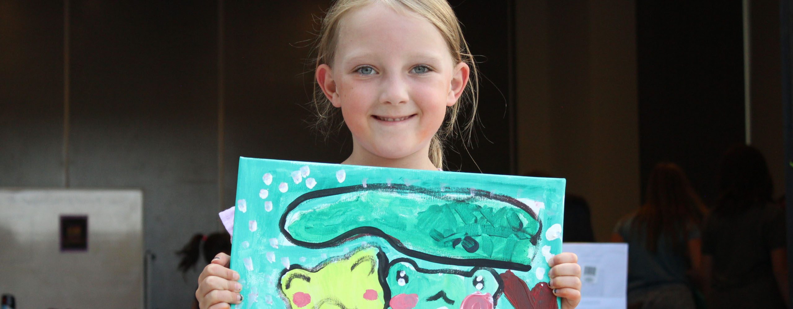 young girl proudly showing off painting of two frogs under a tree