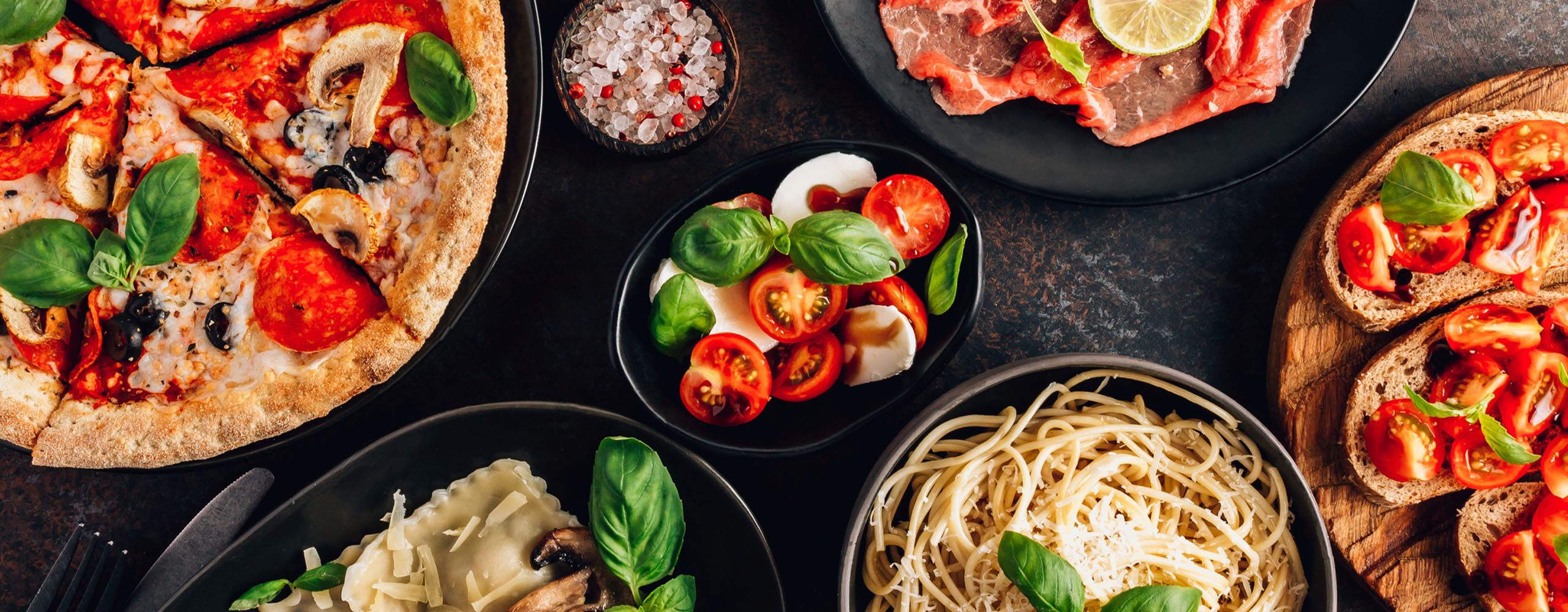 Table of Italian food dishes including pasta, pizza, bruschetta and salad