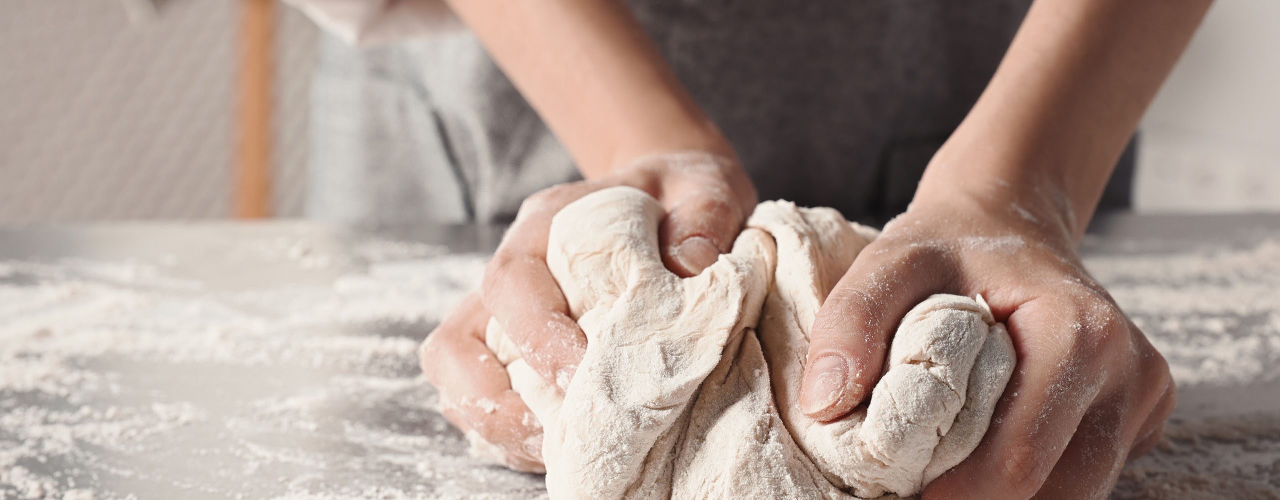 Close up of hands kneading dough on floured work surface