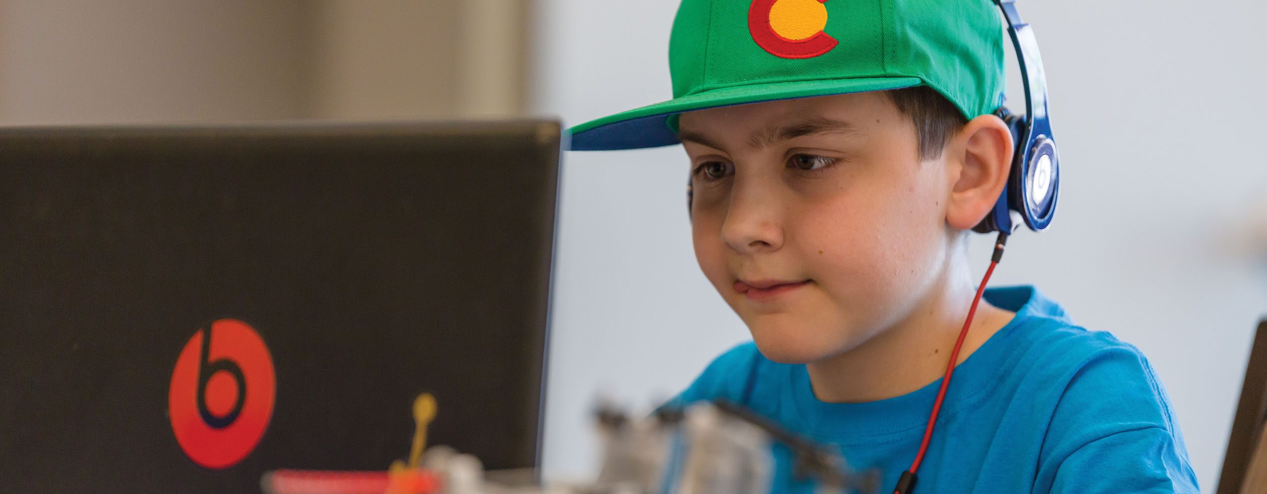 Young boy wearing headphones working at laptop in summer camp classroom