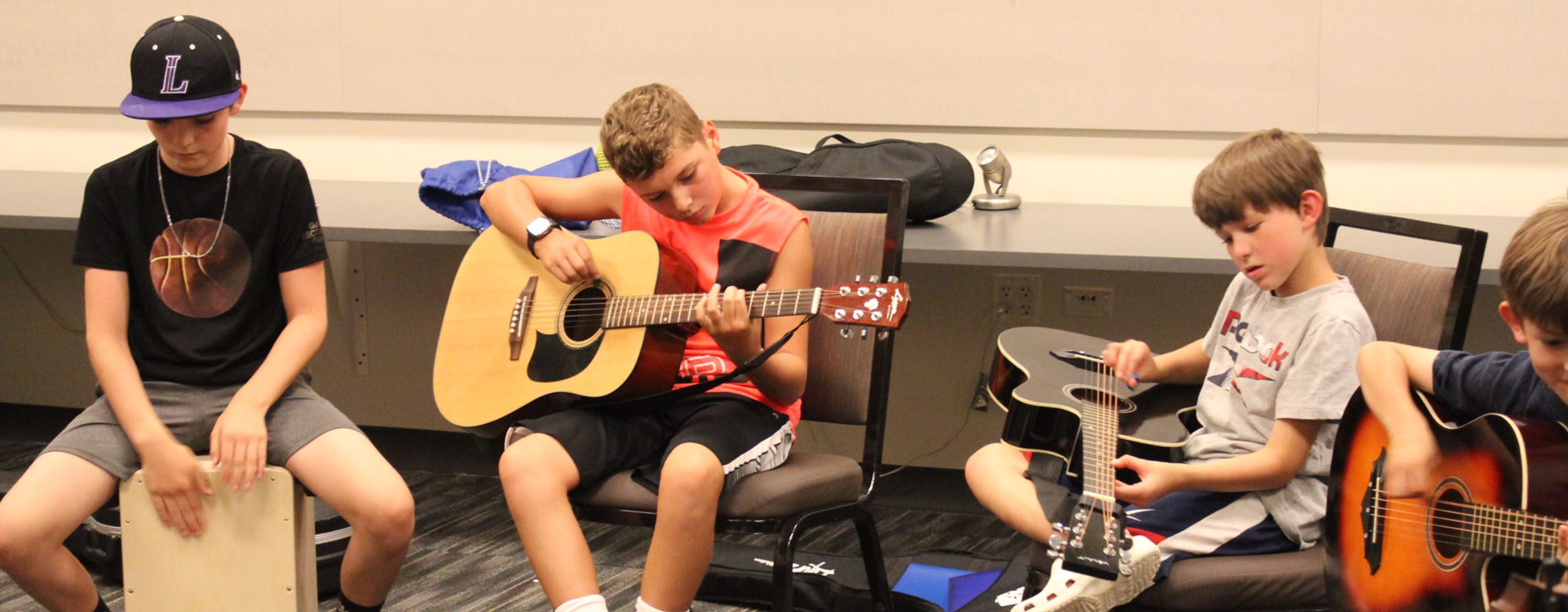 Music - Kids Guitar Class 2560 x 1000 Youth guitar class; younger players sitting in circle with their acoustic guitars